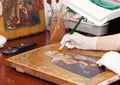 Restorer works on old gilded icon with brush