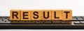 RESULT word made with building blocks. A row of wooden cubes with a word written in black font is located on a black keyboard