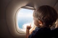 Resumption of flights, opening of borders concept. a small child looks at the ocean from the window of a flying plane. the first Royalty Free Stock Photo