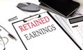 RETAINED EARNINGS text on paper clipboard with chart and notebook on withe background