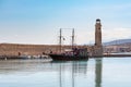 Vintage sailing ship full of tourists is sailing along lighthouse of town harbor.