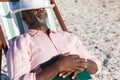 Retired african american senior man sleeping with book and hat over eyes on folding chair at beach Royalty Free Stock Photo