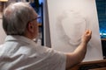 Retired artist sketching creative vase model using pencil on white canvas on wooden easel Royalty Free Stock Photo