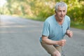 Retired confident male stands on start, ready to take part in sport comeptitions, listens music with earphones and unrecognizable Royalty Free Stock Photo