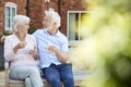 Retired Couple Sitting On Bench With Hot Drink In Assisted Living Facility