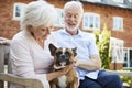 Retired Couple Sitting On Bench With Pet French Bulldog In Assisted Living Facility