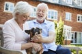 Retired Couple Sitting On Bench With Pet French Bulldog In Assisted Living Facility