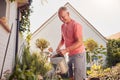 Retired Couple At Work Watering And Caring For Plants In Garden At Home