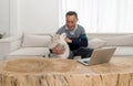 Retired grandfather spending time with his pet in living room at home. Laptop computer are on a table made from large tree trunk Royalty Free Stock Photo