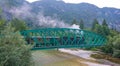 Retired locomotive chugs across the river running through the green mountains. Royalty Free Stock Photo