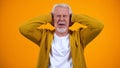 Retired male covering ears by palms displeased with gossips on orange background