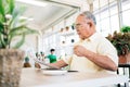 A retired man in casual clothes is concerned with reading a newspaper about COVID-19 news and drinking coffee. Royalty Free Stock Photo