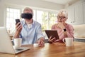 Retired Senior Couple In At Home Using Digital Tablet VR Headset Smartwatch Mobile Phone And Laptop Royalty Free Stock Photo