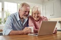 Retired Senior Couple Sitting In Kitchen At Home Drinking Coffee And Using Laptop Royalty Free Stock Photo