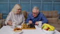 Retired senior couple talking drinking tea, playing chess in modern living home room lounge together Royalty Free Stock Photo