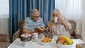 Retired senior couple talking drinking tea, reading book in modern living home room lounge together Royalty Free Stock Photo
