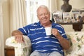 Retired Senior Man Sitting On Sofa Drinking Tea At Home