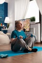 Retired senior woman sitting on yoga mat holding fitness dumbbells in lotus position