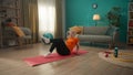 A retired woman lying on a sports mat performs a bicycle exercise. A grayhaired elderly woman takes care of her health