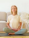 Retired woman meditating and practicing yoga while sitting in lotus pose on floor at home, vertical
