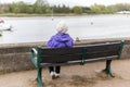 A retired woman sitting alone on a bench sitting out over a river at high tide