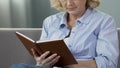 Retired woman sitting on couch and reading book, avid book reader, leisure time