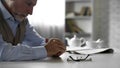 Retiree male sitting alone at kitchen table taken off his glasses, poor vision
