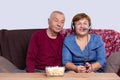 Retirement couple are sitting together on a couch, woman wearing headphones speaking into the microphone. Royalty Free Stock Photo