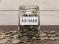 Retirement label on coin jar on top of wooden desk with asorted coins background.