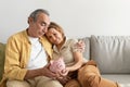 Retirement savings. Senior spouses holding piggybank while sitting together on sofa and embracing, free space Royalty Free Stock Photo