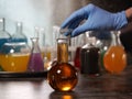 Retort with amber liquid. Hand in glove tube. Laboratory glassware with colorful liquids on the table Royalty Free Stock Photo