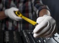 Retractable tape measuring tool in builder hands in white construction gloves over toolbox, closeup.