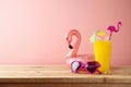 Retro aesthetic 80s concept with orange juice, sunglasses and flamingo pool float on wooden table. Summer vacation vibes