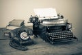 Retro aged black typewriter with paper blank,  telephone, book on wooden table. Vintage style sepia photo Royalty Free Stock Photo