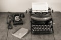 Retro aged black typewriter with paper blank,  telephone, book on wooden table. Vintage style sepia photo Royalty Free Stock Photo