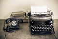 Retro aged black typewriter with paper blank,  telephone, books on wooden table. Vintage style sepia photo Royalty Free Stock Photo