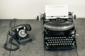 Retro aged black typewriter with paper blank,  telephone on wooden table. Vintage style sepia photo Royalty Free Stock Photo