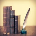 Retro aged books, quill pen and inkwell on oak wooden table. Vintage style filtered photo