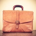 Retro aged leather briefcase on oak wooden table. Vintage style sepia photo