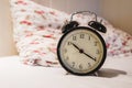 Retro alarm clock with 10 O`clock and twenty minuet, on white bed with pillow Royalty Free Stock Photo