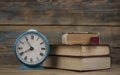 Retro alarm clock and stack of old books over wooden wall background Royalty Free Stock Photo