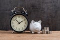 Retro alarm clock with white piggy bank and stack of coins on wooden table and black background as long term savining money or re Royalty Free Stock Photo