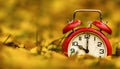 Retro alarm clock in yellow gold autumn leaves, daylight savings time background Royalty Free Stock Photo