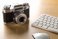 Retro analog SLR camera next to computer keyboard and mouse on wooden desk in office, digital photography or image processing