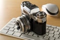 Retro analog SLR camera on top of computer keyboard and mouse on wooden desk in office, digital photography or image processing