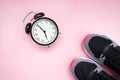 Retro black alarm clock and black with raspberry sneakers on a pink background. The concept of doing sports, yoga, fitness at home Royalty Free Stock Photo