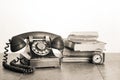 Retro black telephone and books, clock on old oak wooden table. Vintage style sepia photo