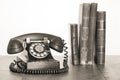 Retro black telephone and books on old oak wooden table. Vintage style sepia photo