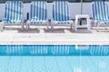 Retro blue and white sunbeds on the poolside of a swimming pool filled with clear blue water at the garden of a holiday Royalty Free Stock Photo