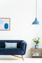 Retro bowl pendant light and a baby blue cushion on a dark, elegant sofa in a simple living room interior with white walls. Real p